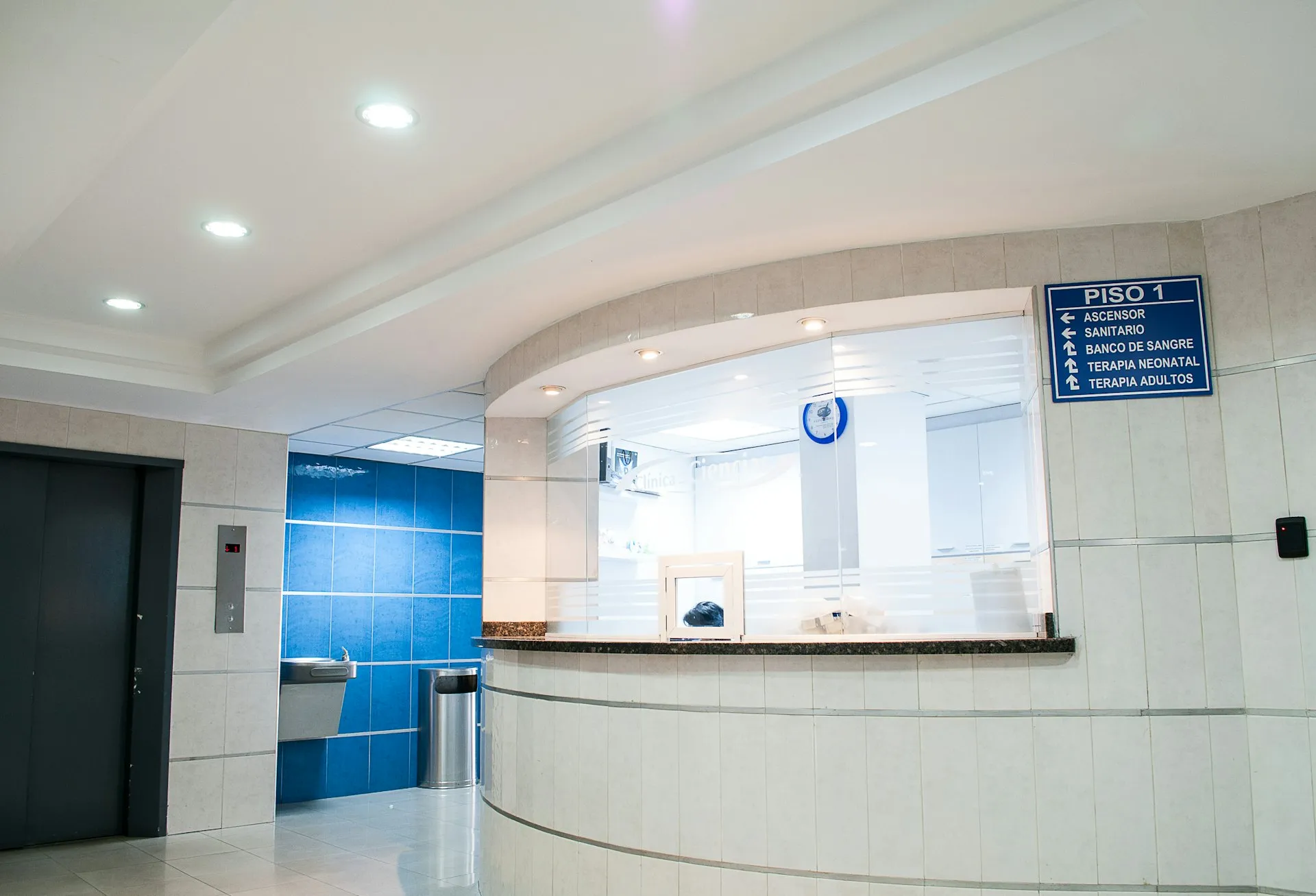 Quầy tiếp đón bệnh viện với ô kính lớn và bảng chỉ dẫn các khoa treo trên tường